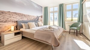 Una camera da letto con un letto, un comodino, una sedia e vista su un edificio attraverso una finestra.