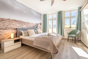 A bedroom with a bed, nightstand, chair, and a view of a building through a window.