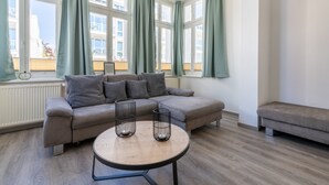 Un soggiorno moderno con un divano grigio, un tavolino rotondo e vista su un edificio attraverso ampie finestre.