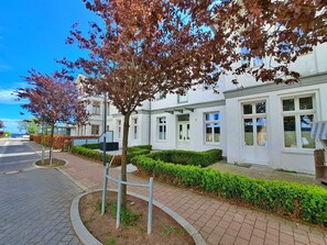 A residential building with a paved walkway, neatly trimmed hedges, and a tree with autumn leaves.