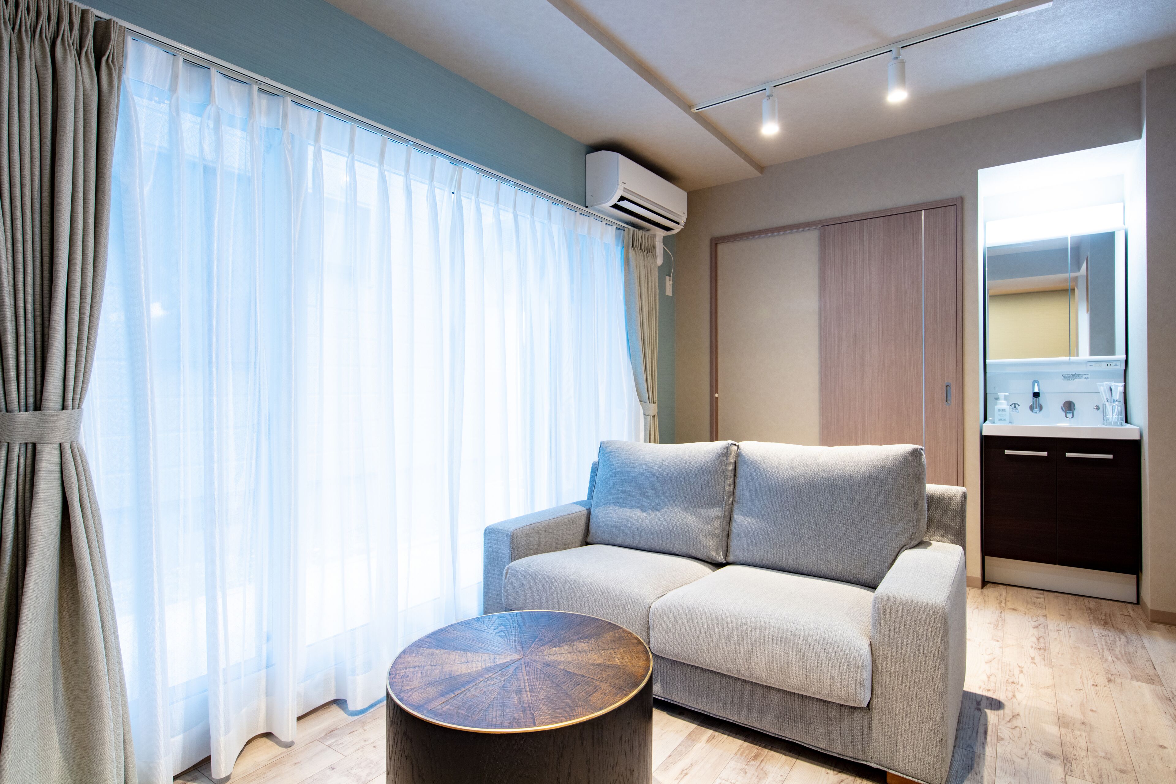Un salon moderne avec un canapé, une table basse ronde et un coin cuisine équipé de placards et d’un évier.