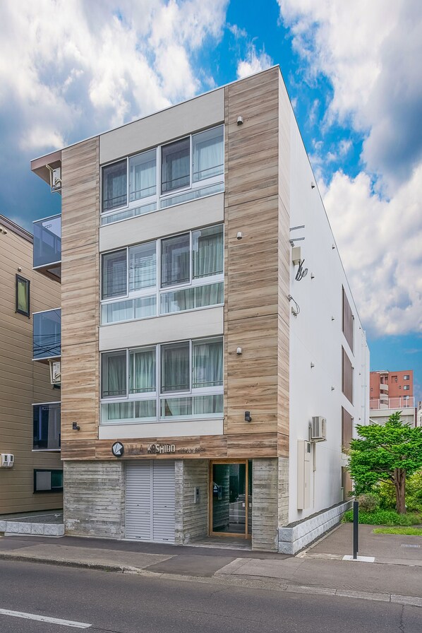 Un immeuble à plusieurs étages au design moderne, caractérisé par un mélange de matériaux, notamment du bois et du béton, de grandes fenêtres et une entrée bien visible avec une porte de garage.