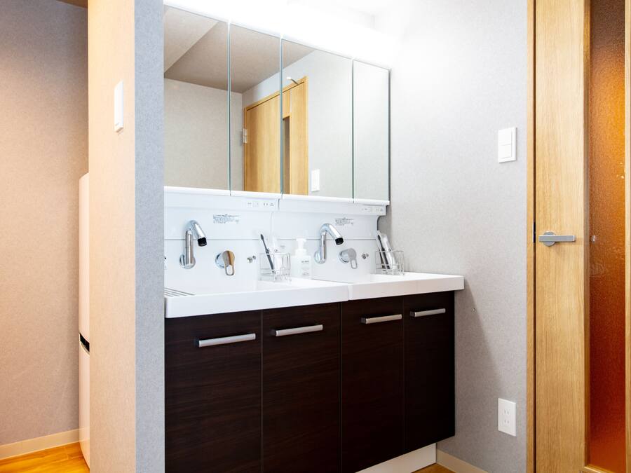 Un baño moderno con lavamanos doble, armarios de madera oscura y un espejo grande sobre el lavamanos.
