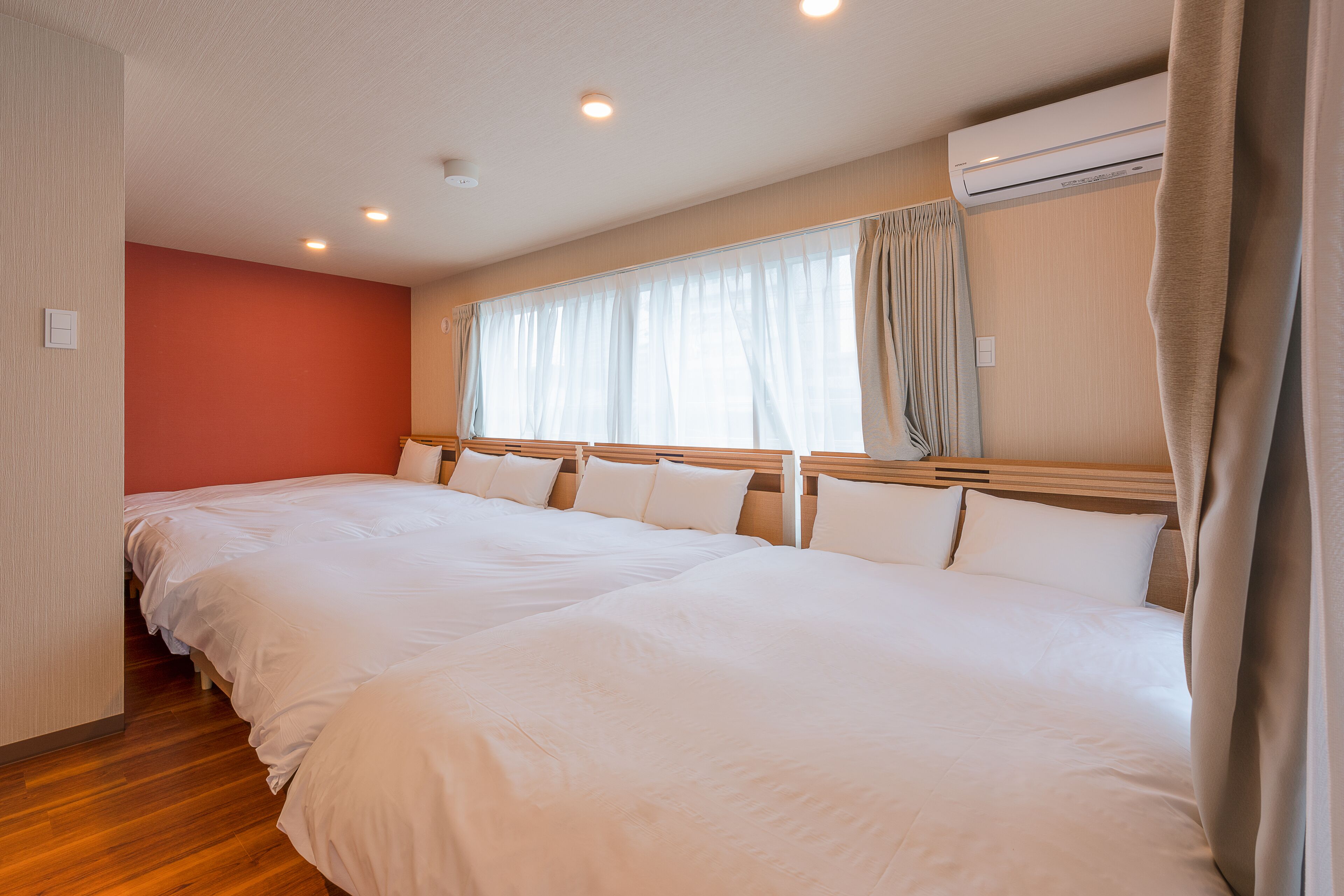 A hotel room with two large beds, a wooden headboard, a window with curtains, and an air conditioning unit.