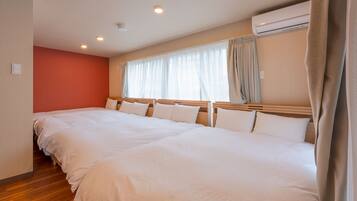 A hotel room with two large beds, a wooden headboard, a window with curtains, and an air conditioning unit.