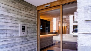 A wooden exterior wall with a glass door entrance, a reception desk, and a blue mat with text.
