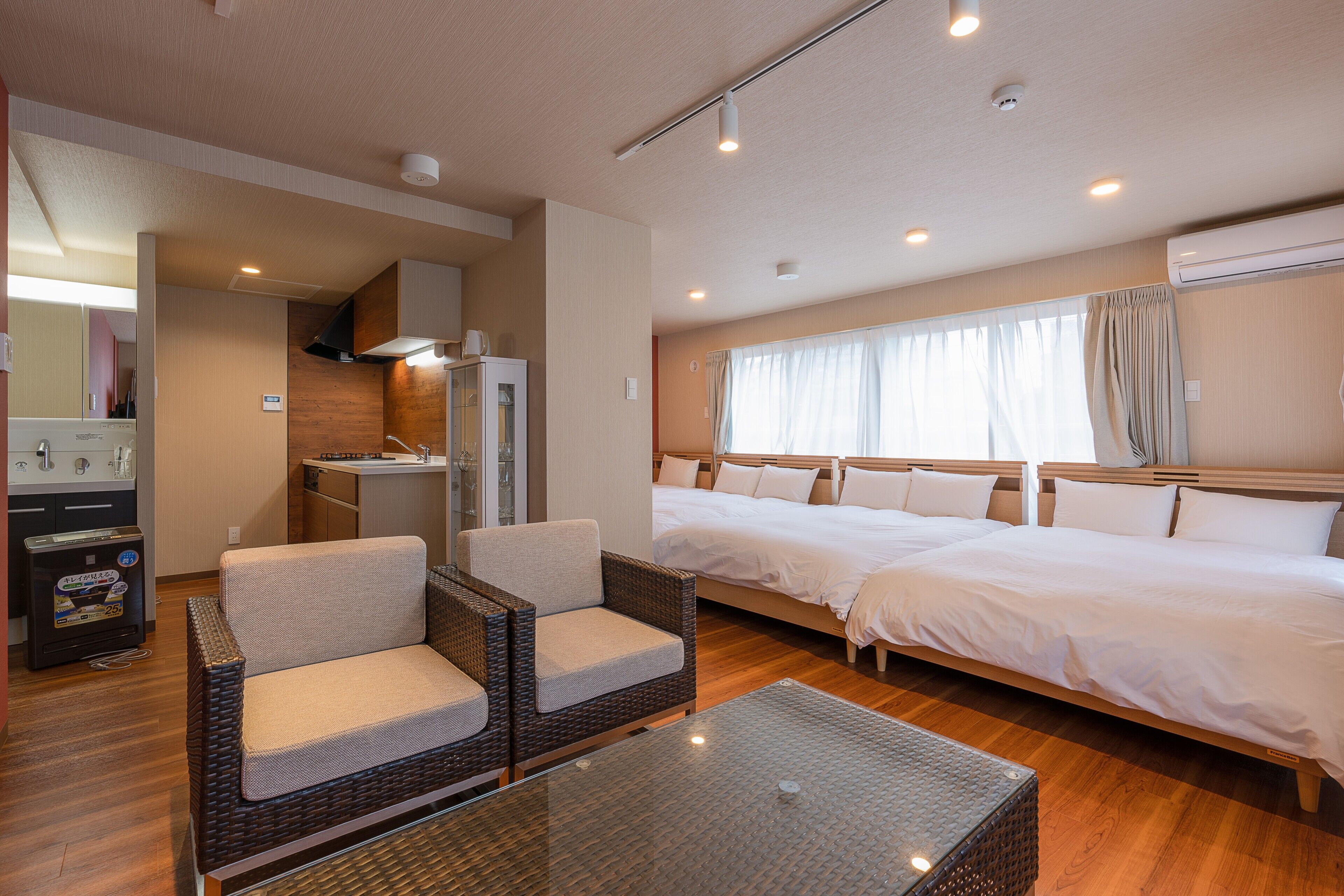 Een hotelkamer met een bed, twee stoelen, een tafeltje, een kitchenette en een raam met gordijnen.
