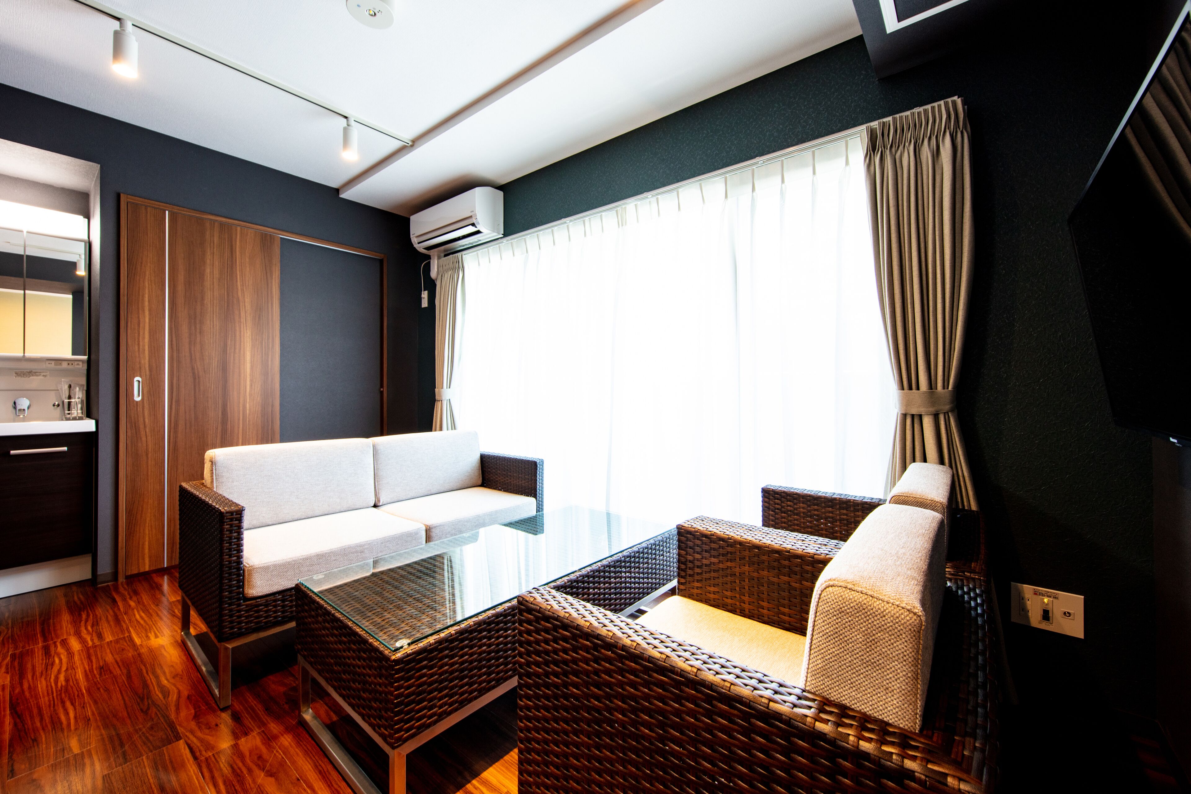 A modern room with a glass table, wicker furniture, a white sofa, and a large window with curtains.