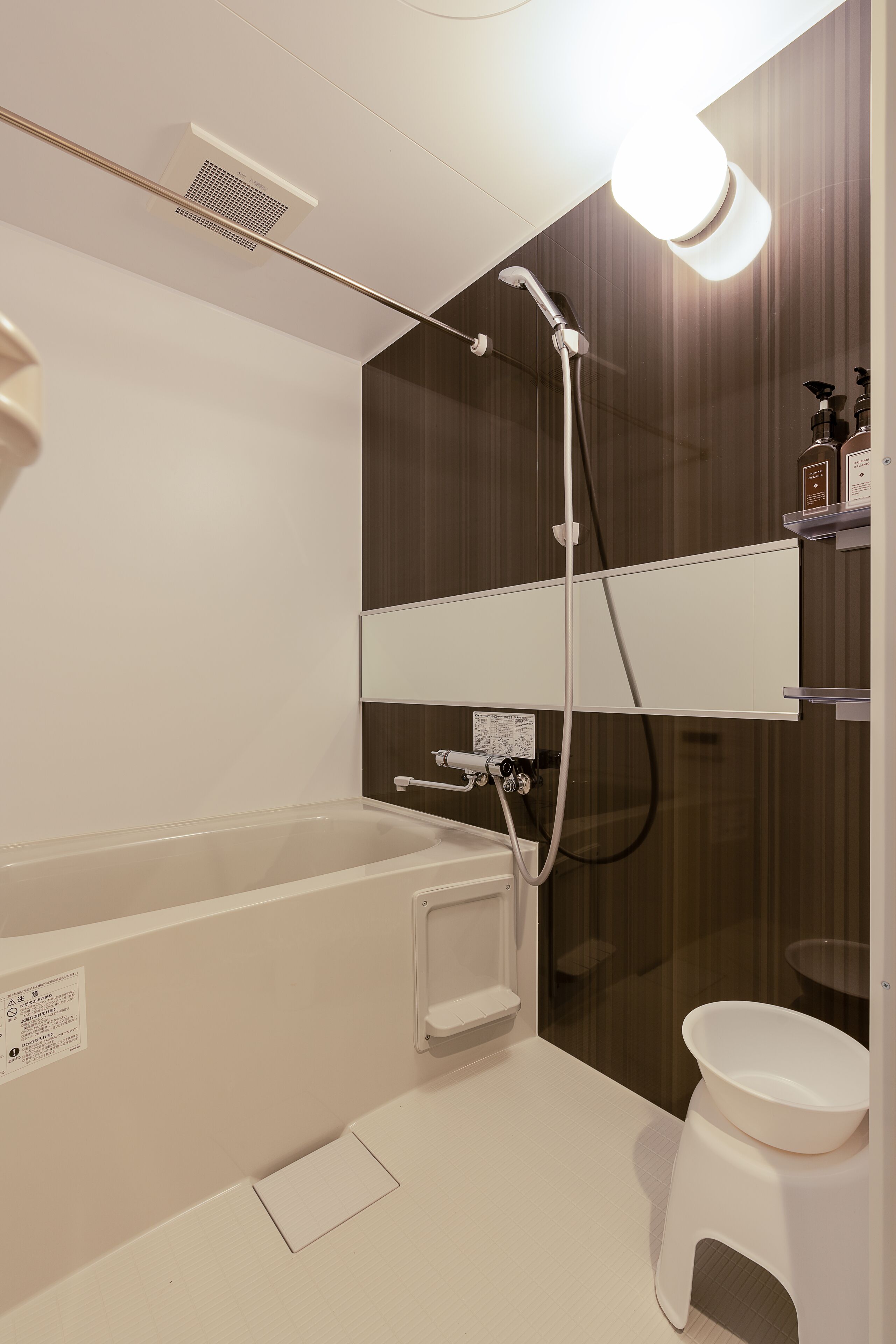 Un baño moderno con bañera, inodoro y ducha. Hay repisas con artículos de aseo y una lámpara sobre la ducha.