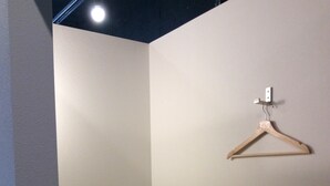 A small, dimly lit room with a single bed, a wooden hanger on the wall, and a light fixture above. - bnb Atami Resort - Hostel (Atami)