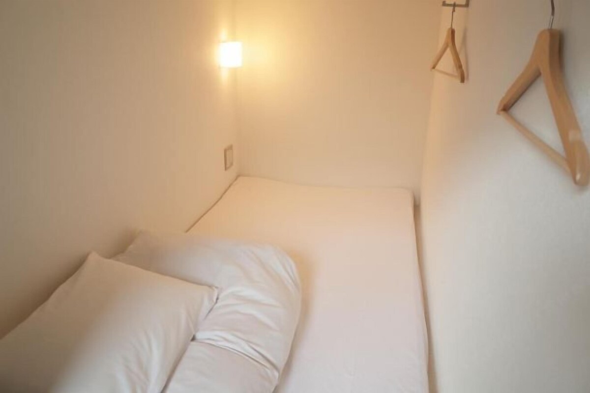 Una habitación pequeña con cama individual, una mesita de noche y una lámpara fijada a la pared.