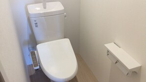 A small, white toilet with a tank and a flush handle, a visible water inlet, and a white flush tank on the right. - bnb Atami Resort - Hostel (Atami)