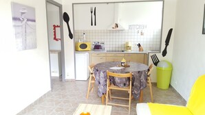 A compact kitchen with white cabinets, a microwave, a toaster, and a coffee maker. There is a dining table with chairs and a yellow chair. - Vacation house 4 persons (ARCANGUES)