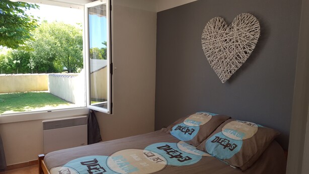 A bedroom with a bed, a window, and a heart-shaped wall decoration. - Vacation house 4 persons (ARCANGUES)