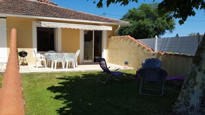 A patio with a table and chairs, a barbecue grill, and a covered area with a striped awning. - Vacation house 4 persons (ARCANGUES)