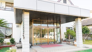 A modern building with a glass entrance, a covered patio area, and a well-maintained garden. - Tabist Watanabe Chiba Ichinomiya (Ichinomiya)