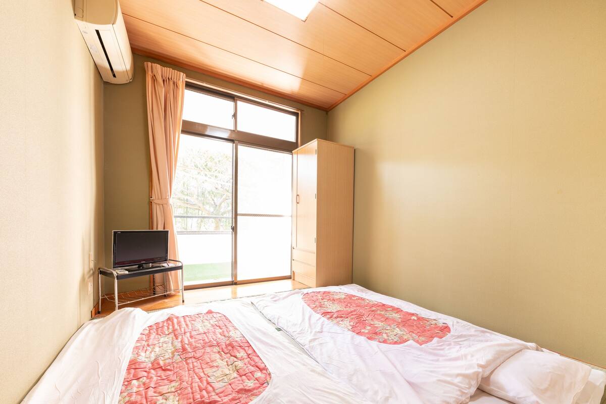 Une chambre à coucher avec un lit, un téléviseur posé sur un meuble, une armoire et une porte-fenêtre coulissante donnant sur l’extérieur.