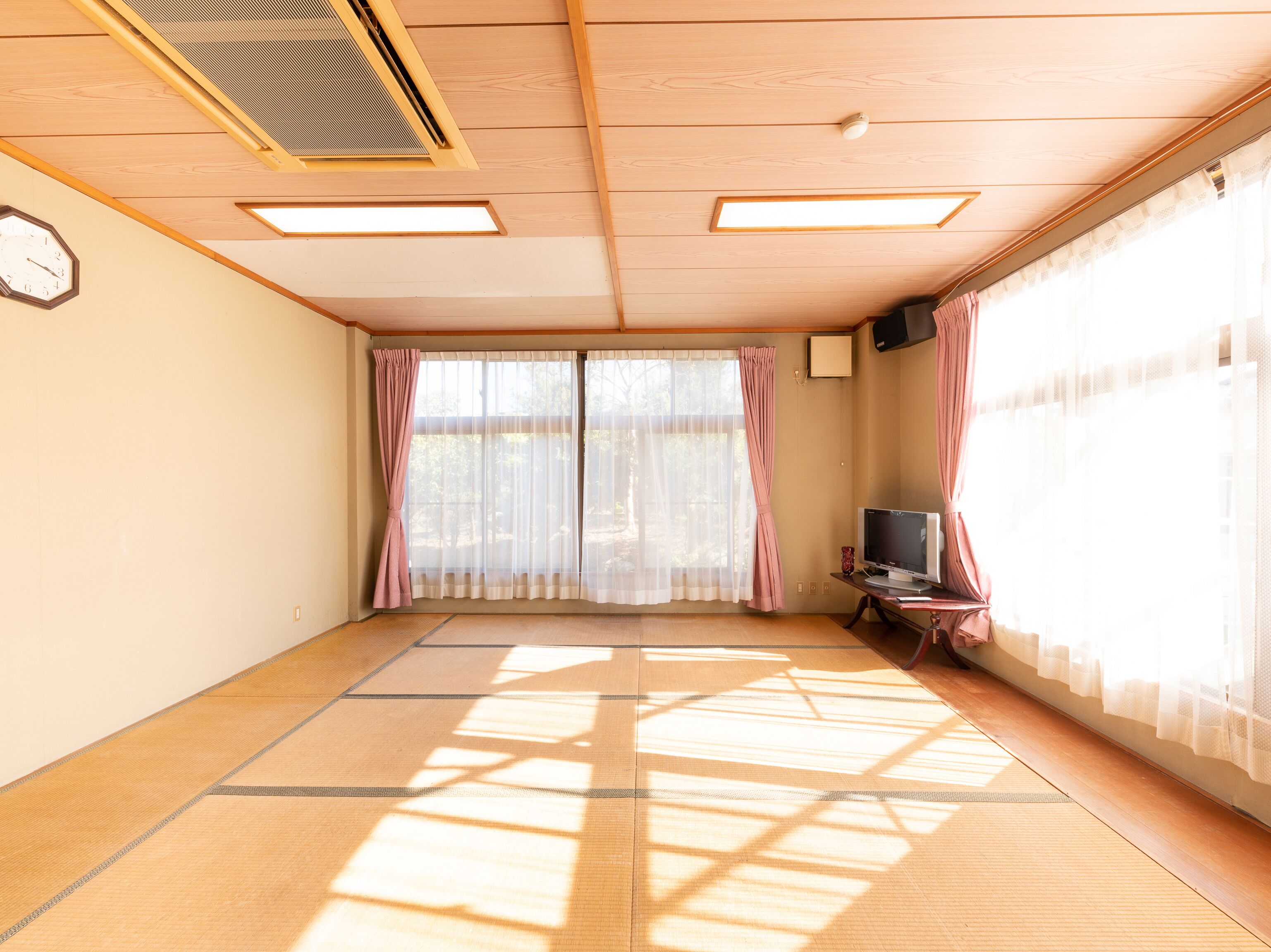 Una stanza con pavimento in tatami, una televisione su un supporto e un'ampia finestra con tende leggere.