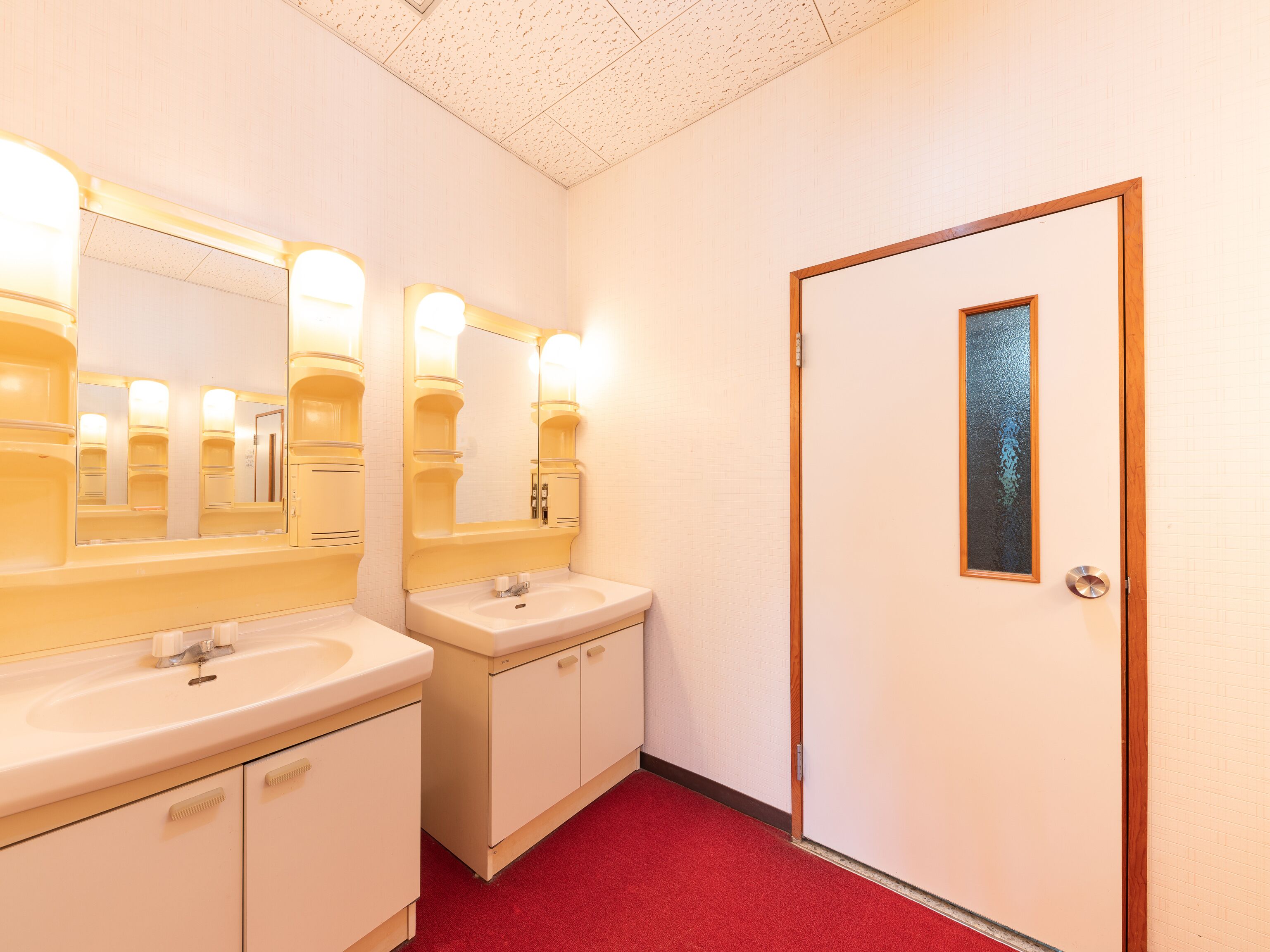 A hotel bathroom with two sinks, mirrors, and a door with a frosted glass panel.