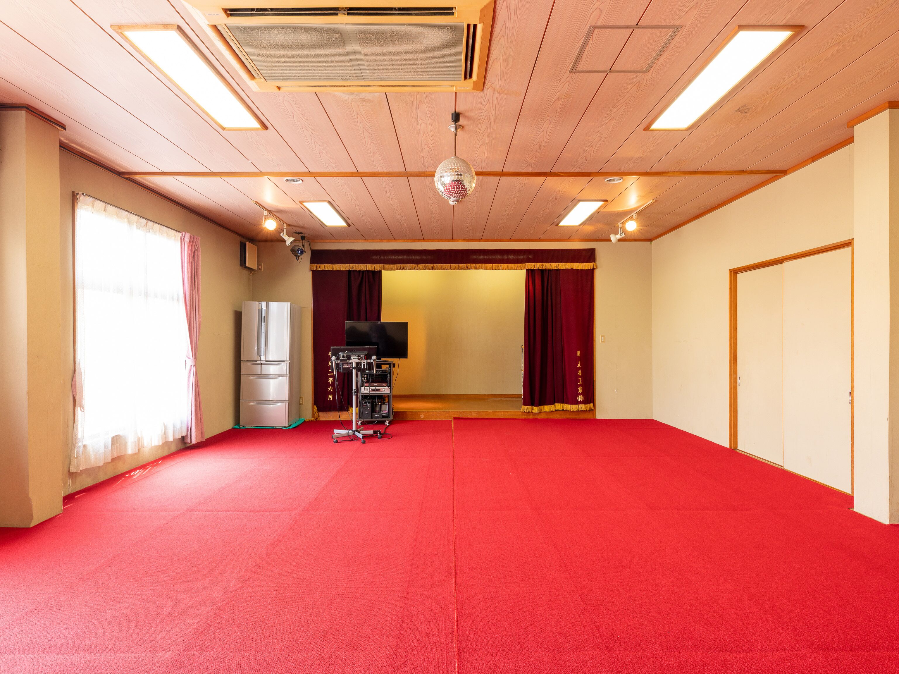 Una habitación amplia con alfombra roja, techo de madera y un televisor de pantalla plana grande.