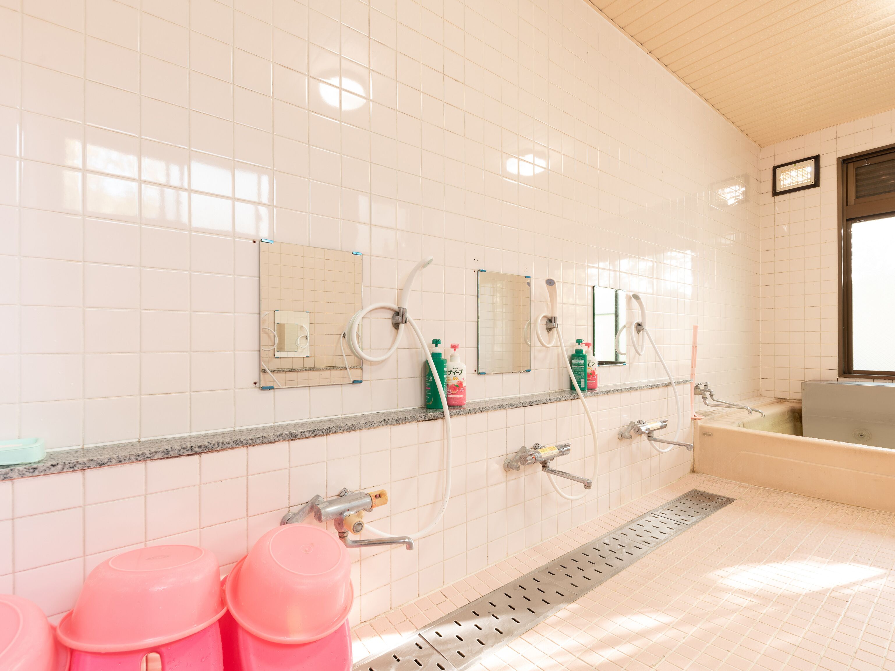A bathroom with white tiled walls, multiple sinks, mirrors, and a window.