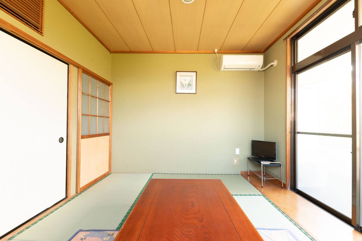 Une pièce de style japonais traditionnel, avec un sol recouvert de tatamis, une porte coulissante, un téléviseur et un appareil de climatisation.