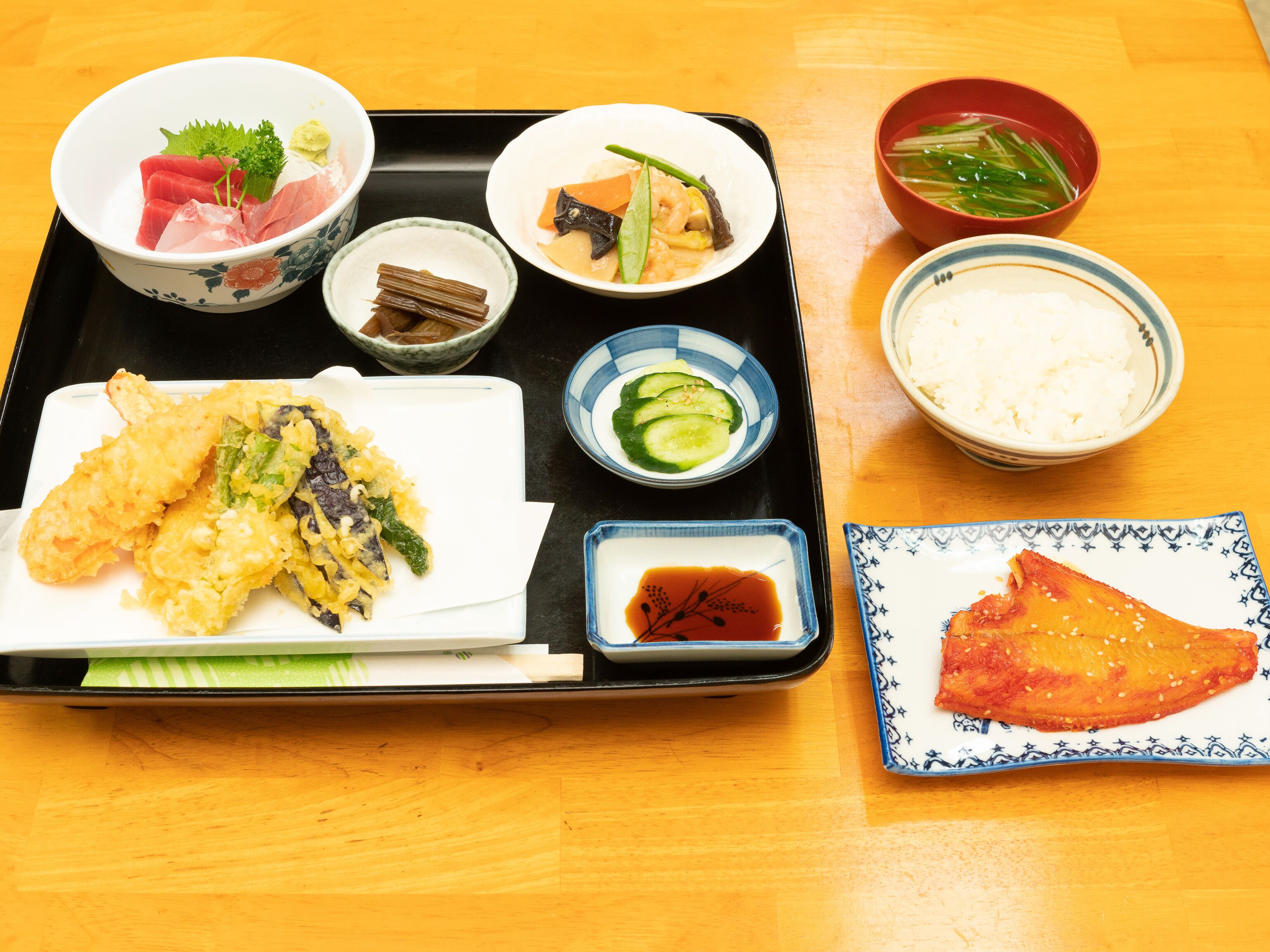 A tray with various Japanese dishes including sushi, tempura, and rice.