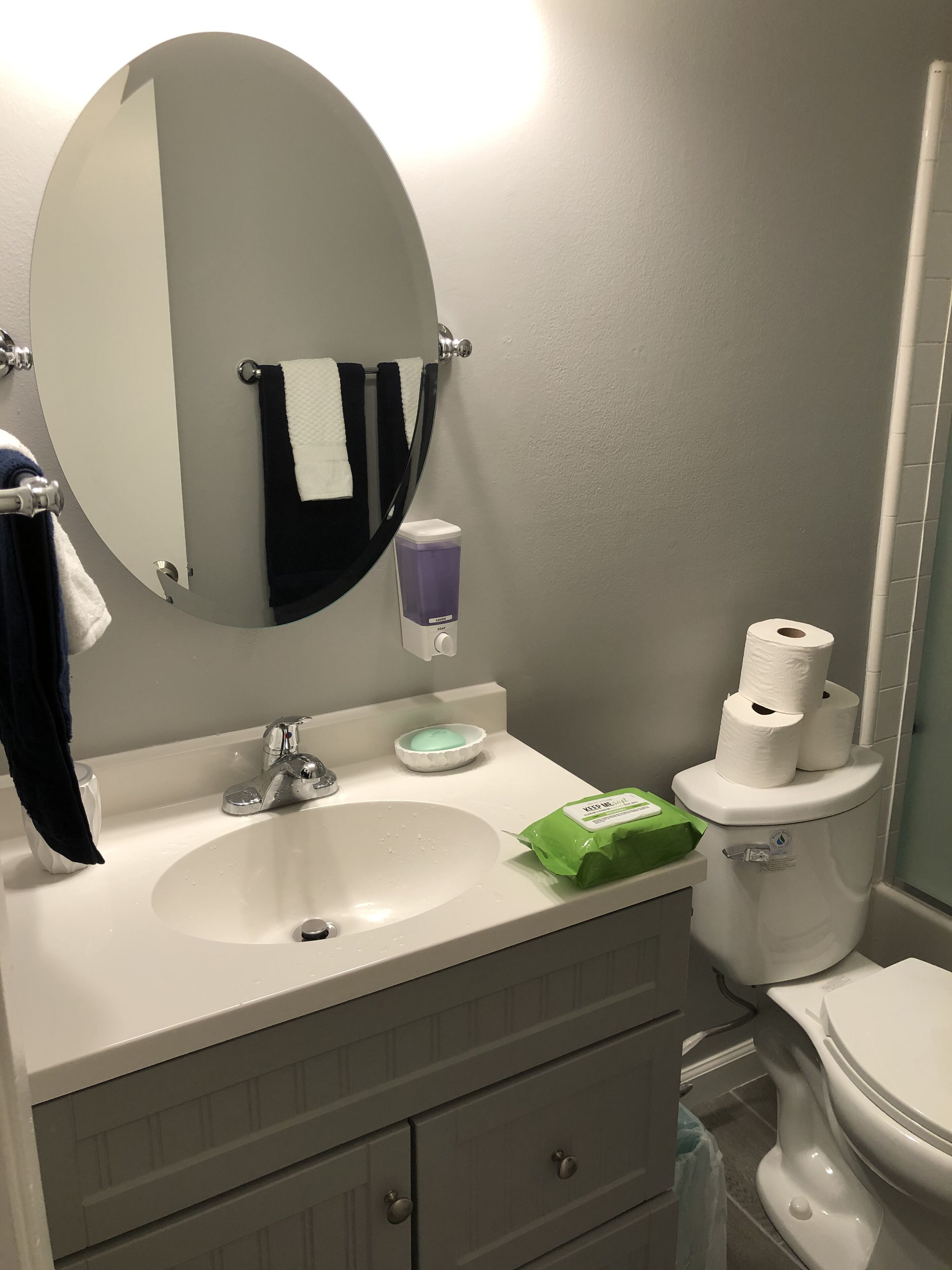 Ein Badezimmer mit rundem Spiegel, Waschbecken, Toilette und Handtuchhalter.