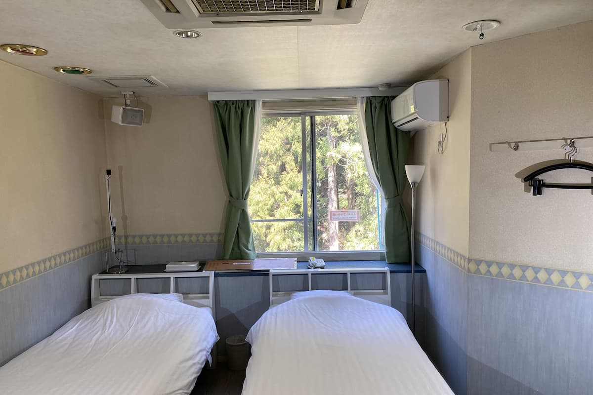 Una habitación con dos camas, una ventana con cortinas, un escritorio con computadora y un aire acondicionado.