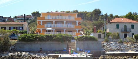 A multi-story building with balconies, situated by a waterfront with a dock.