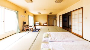 Une pièce de style japonais traditionnel, avec un sol recouvert de tatamis, un futon servant de lit, une télévision et des portes coulissantes.