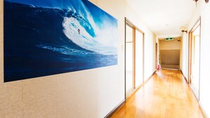 Un couloir avec une grande peinture représentant une vague sur le mur, un plancher en bois et des portes donnant sur différentes pièces.