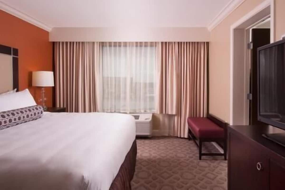 A hotel room with a bed, a television, a desk, and a window with curtains.