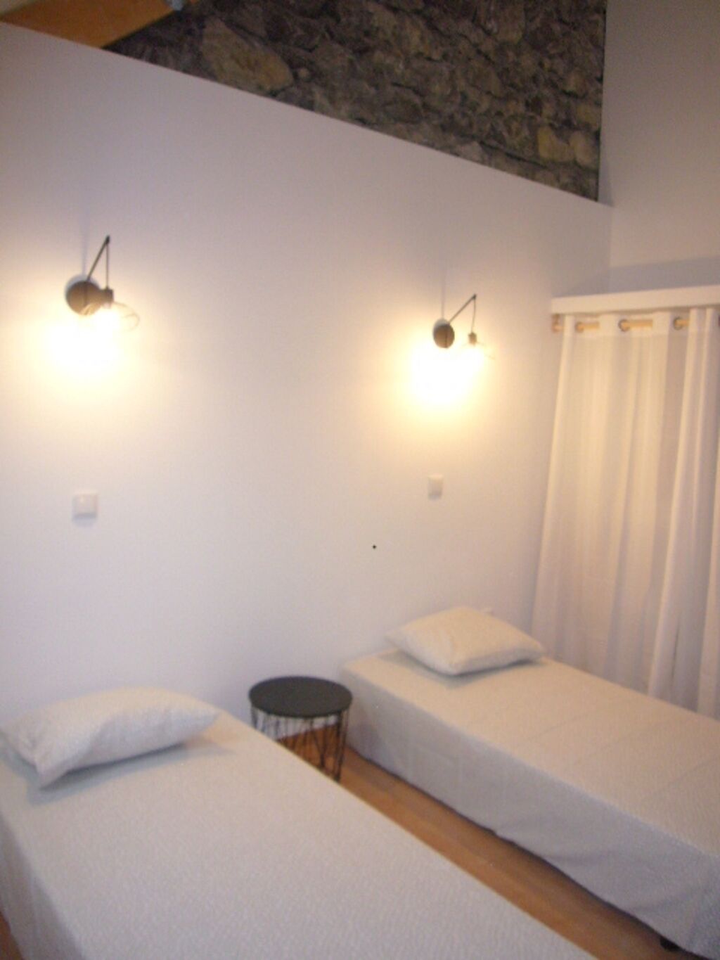 A room with two single beds, a small round table, and two wall-mounted light fixtures.
