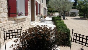 Un edificio de piedra con contraventanas rojas, un camino pavimentado y un jardín bien cuidado con arbustos y flores.