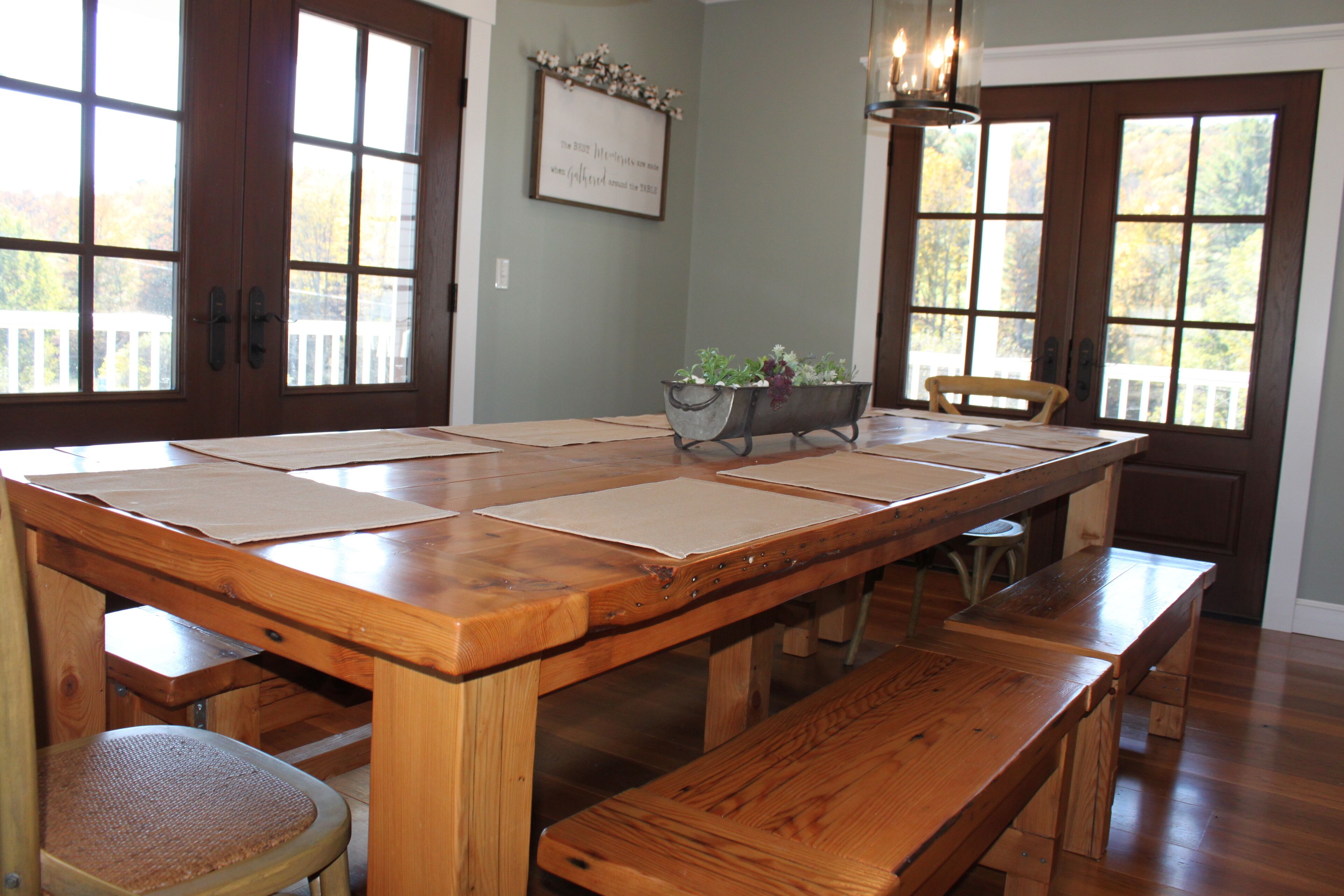 A wooden dining table with four benches, a metal planter with plants, and a framed sign on the wall.