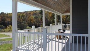 Une véranda couverte avec des balustrades blanches, un plafond en bois et une vue sur une colline boisée.