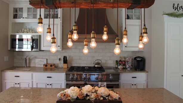 Une cuisine avec des meubles blancs, un réfrigérateur en acier inoxydable, une cuisinière à gaz et des luminaires suspendus.