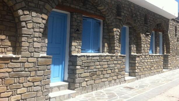 A stone building with blue doors and shutters, featuring a traditional architectural style with arched windows and a stone facade. - Louiza Hotel (Paros)