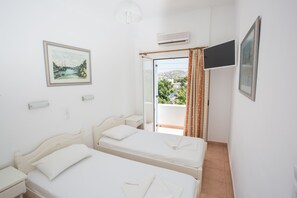 Ein Schlafzimmer mit zwei Betten, einem fensterbelaubten Fenster, einer Wand-Klimaanlage und einem gerahmten Bild.