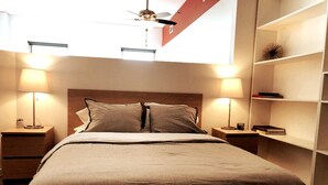 Ein ordentlich bezogenes Bett mit einem hölzernen Kopfteil, zwei Nachttischlampen und einem Regal mit Büchern und einem Dekorationsobjekt.