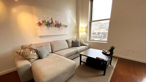 Ein modernes Wohnzimmer mit einer Eckcouch, einem Couchtisch und einem großen Fenster mit Blick auf die Skyline.