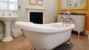 A bathroom with a freestanding bathtub, a pedestal sink, a vanity with a mirror, and framed pictures on the wall. - Westgate Manor (Bishop Auckland)