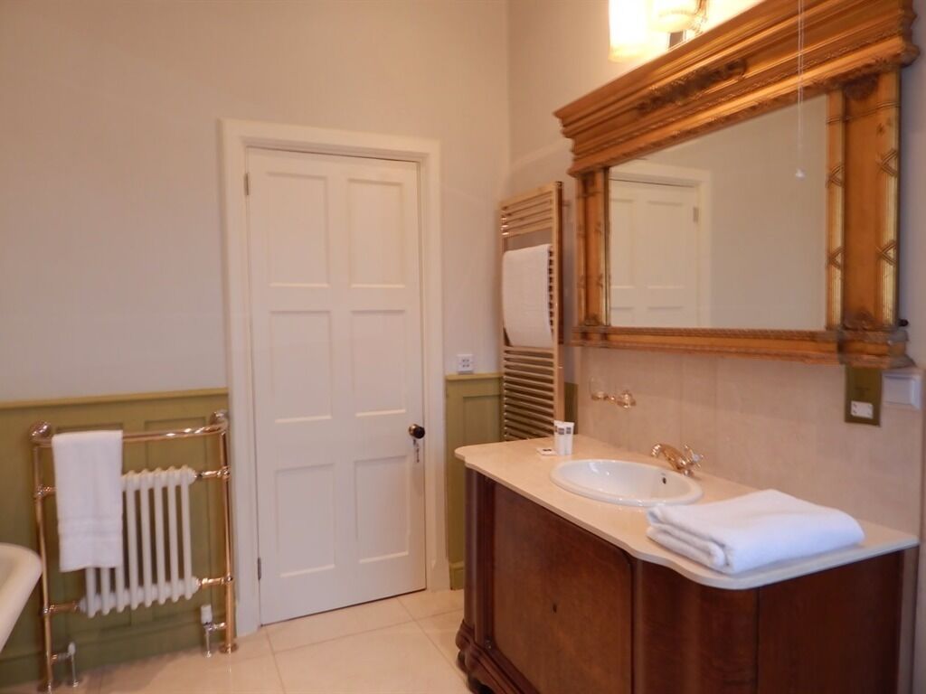 A bathroom with a white door, a radiator, a wooden vanity with a sink, and a large mirror.