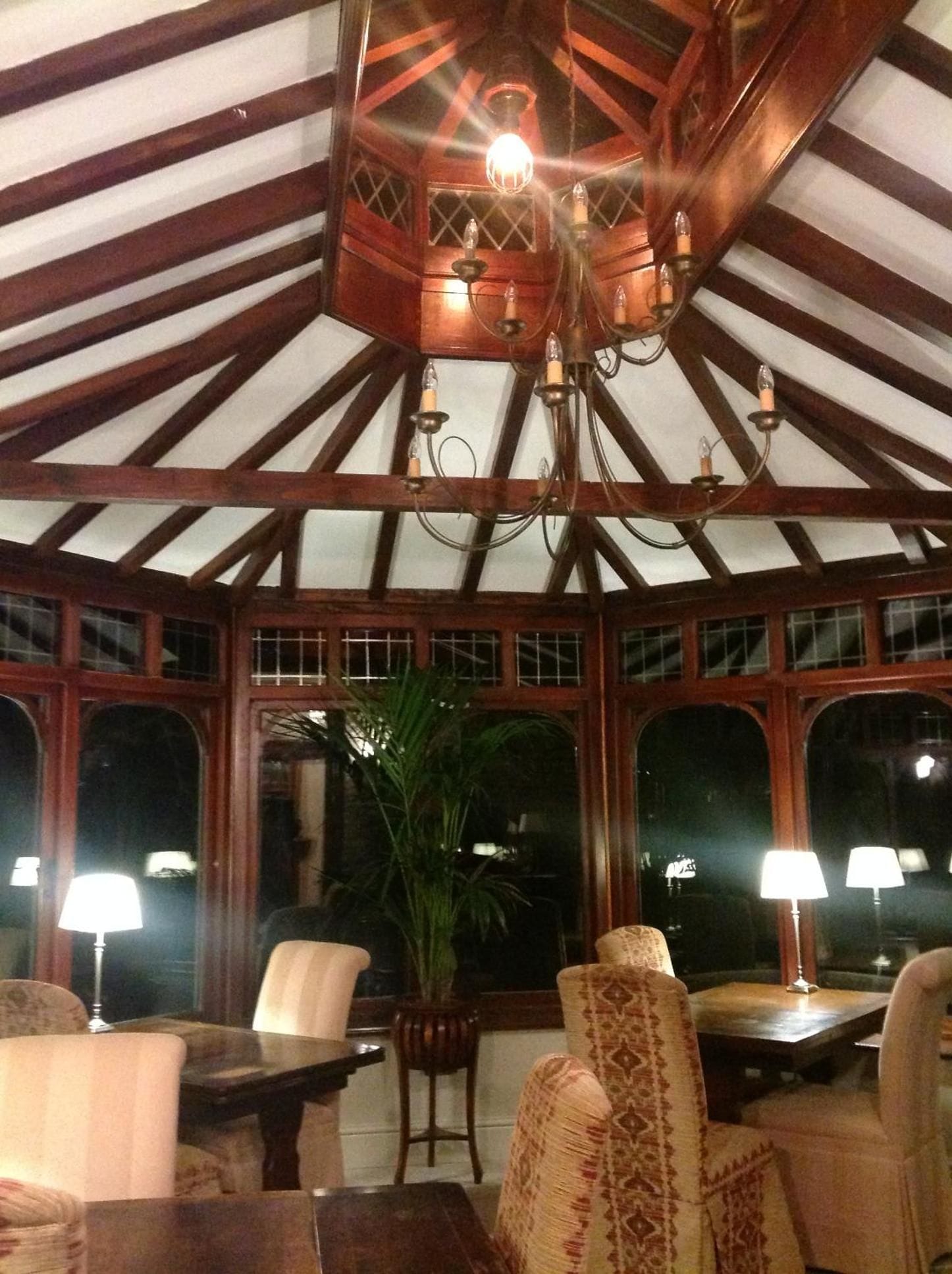A covered patio area with wooden beams, a chandelier, and seating arrangements.