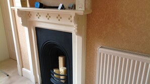 A room with a fireplace, a radiator, and a shelf with items. - Westgate Manor (Bishop Auckland)