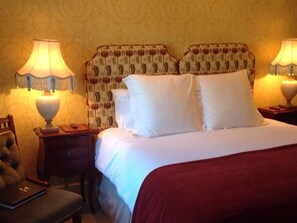 Una habitación de hotel con una cama, dos mesitas de noche, una lámpara, una silla y una pequeña mesa con un libro.
