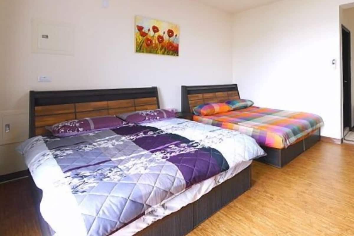 A bedroom with two beds, a wooden floor, and a painting on the wall.