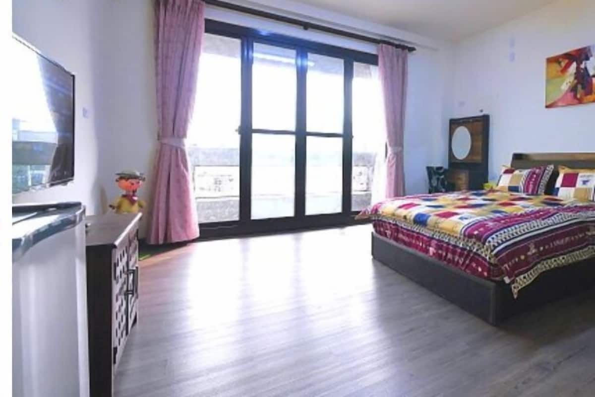 A bedroom with a bed, a dresser, a television, and a window with curtains.