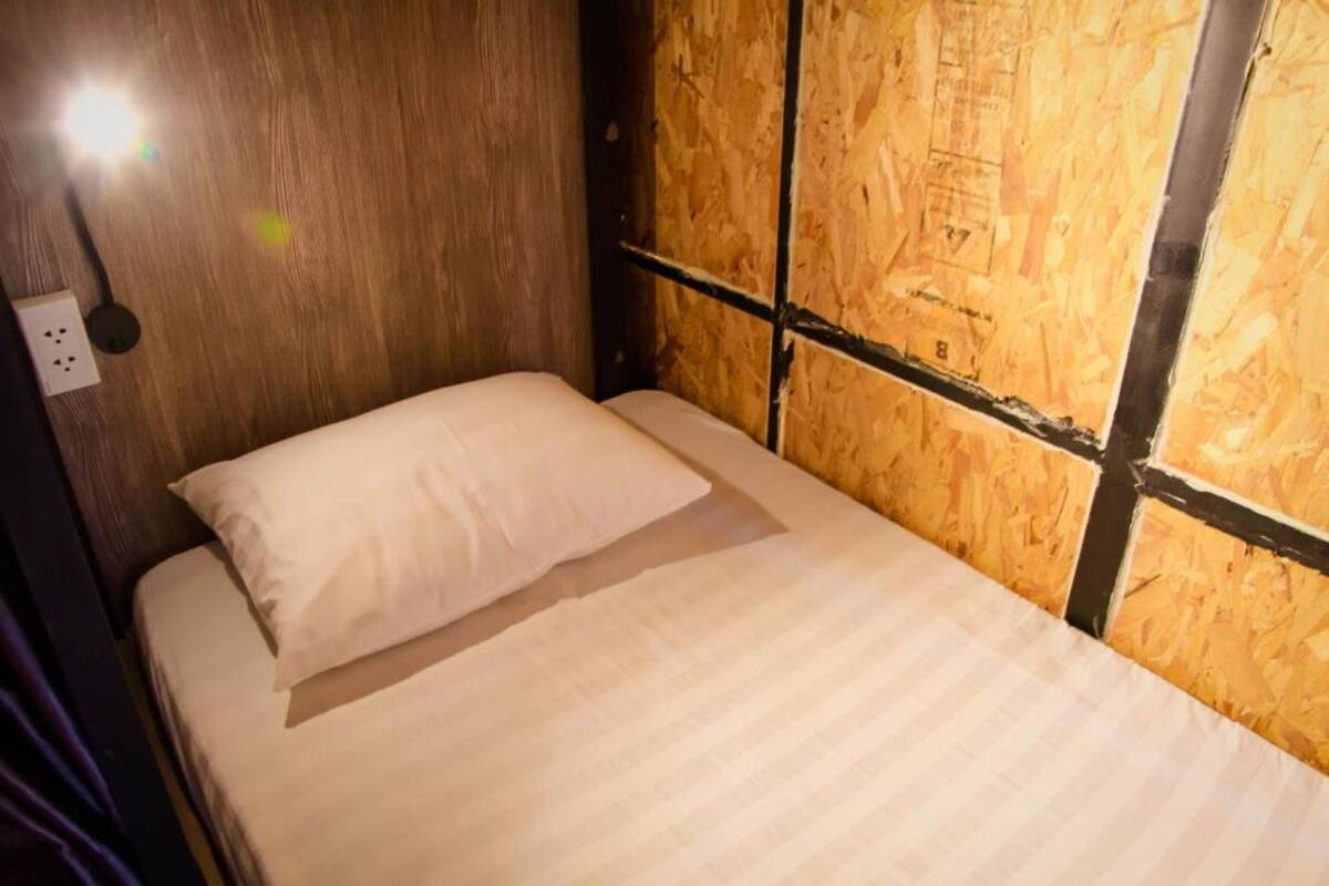 A single bed with a white pillow in a room with wooden paneling and exposed insulation.